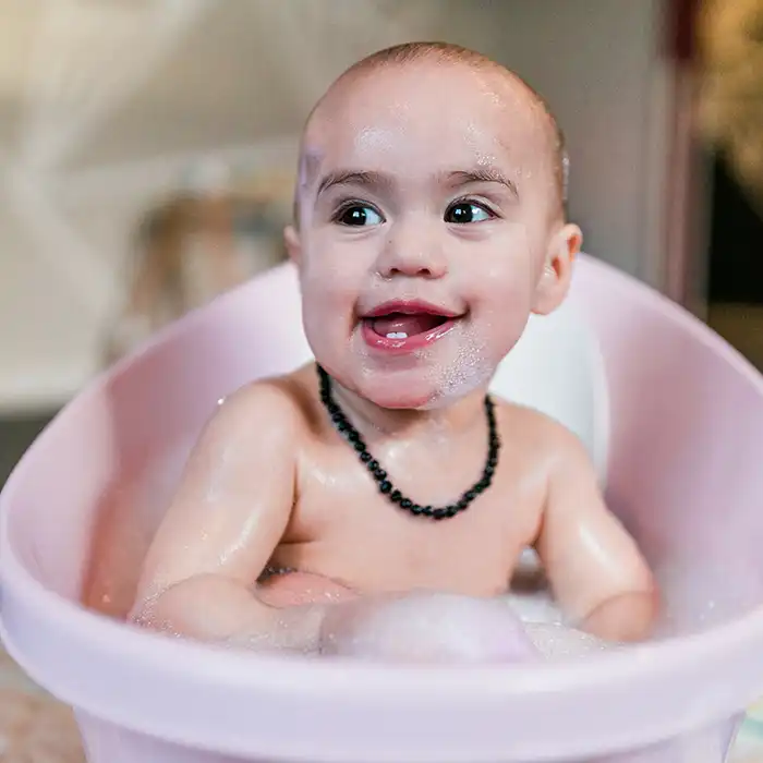 A smiling baby sitting up in a small bath. 
