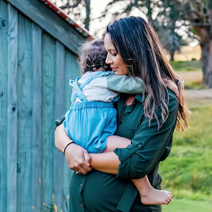 Pregnant mother holding child in front of shed