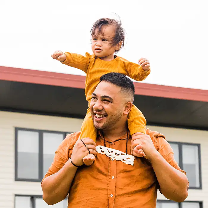 A smiling adult carrying a child on their shoulders. 
