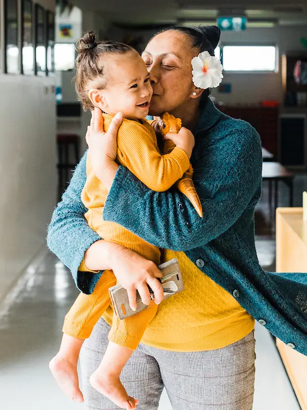 A photo of an adult standing, holding a toddler and kissing them. 