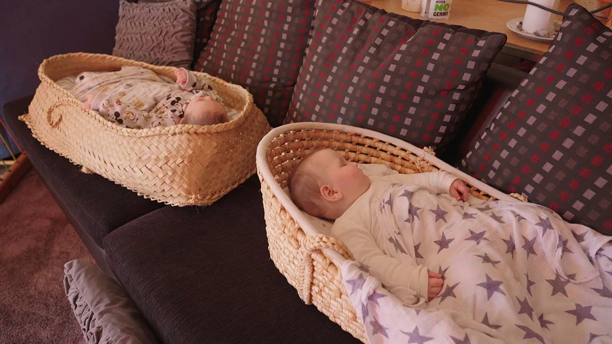 Two babies lying in two wahakura placed on a couch.