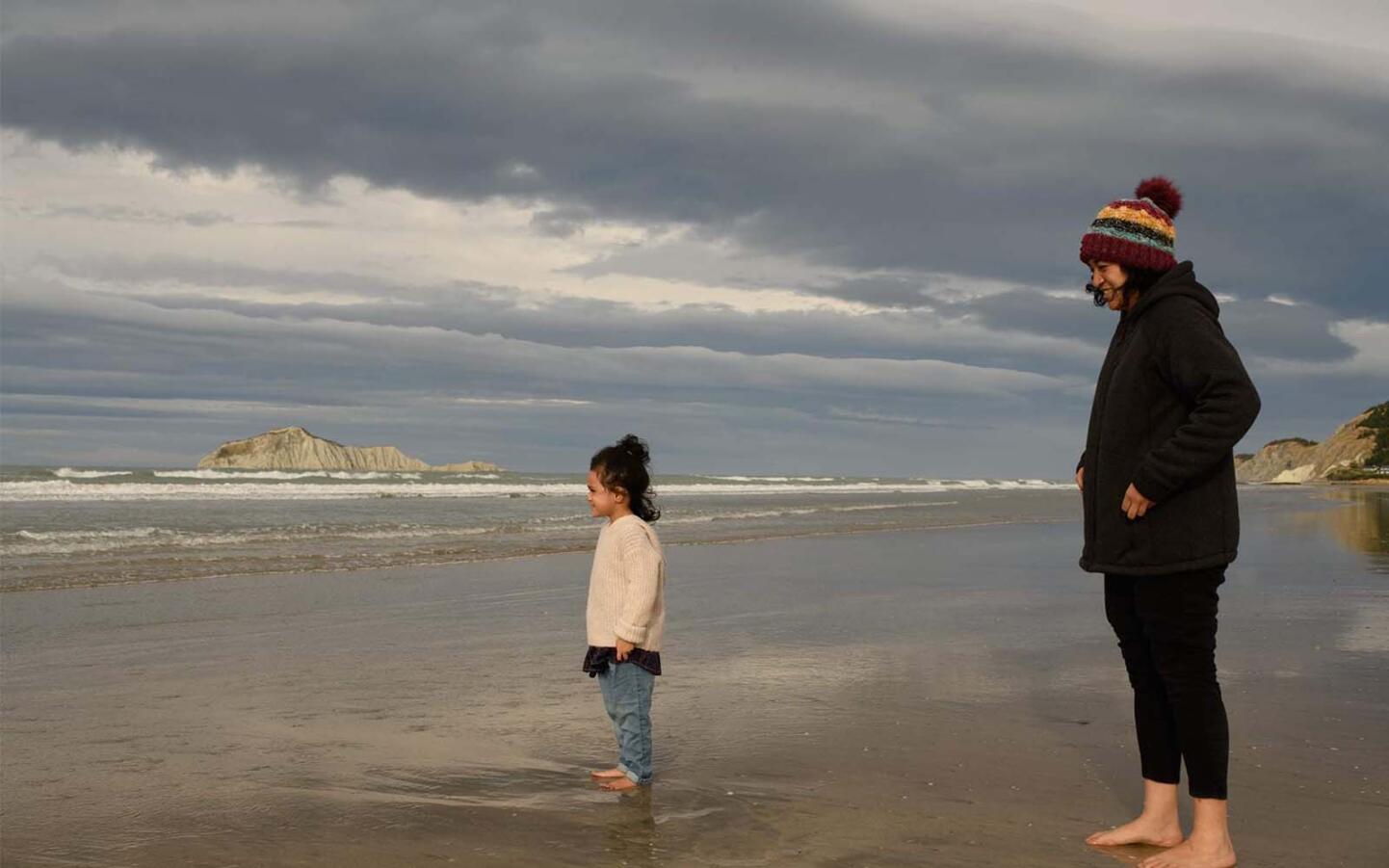 Mother and daughter on beach looking out at the ocean.