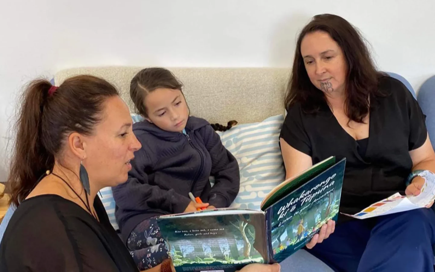 Two women reading a book to a young girl. 