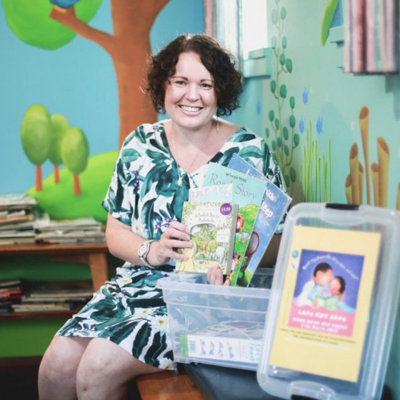 A smiling woman holds several books on display.