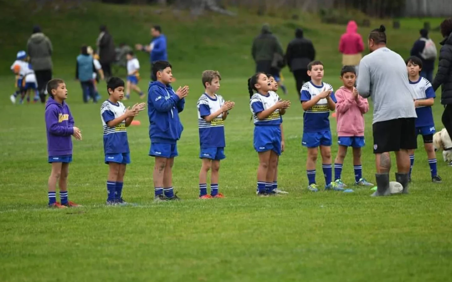 Daniel Filemoni coaches a group of young rugby players, lined up on a grassy field.