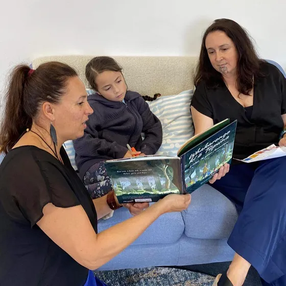 Two women reading a book to a young girl.