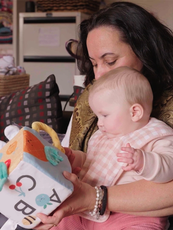 Moana Walford with baby on her lap, playing with toy.