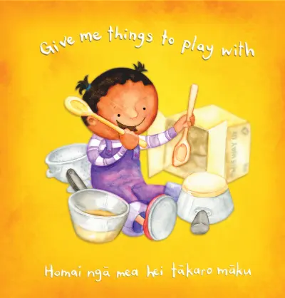 A young child sits on the floor, merrily banging on pots and pans with a wooden spoon. Text reads: "Give me things to play with / Homai ngā mea hei tākaro māku."