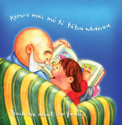 An older adult shows photos to a young child sitting beside them in a chair. Text reads: "Teach me about our family / Kōrero mai mō tō tatou whānau."