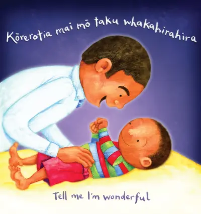 A father leans lovingly over a baby lying on their back on a mat. Text reads: Tell me I'm wonderful / Kōrerotia mai mō taku whakahirahira."